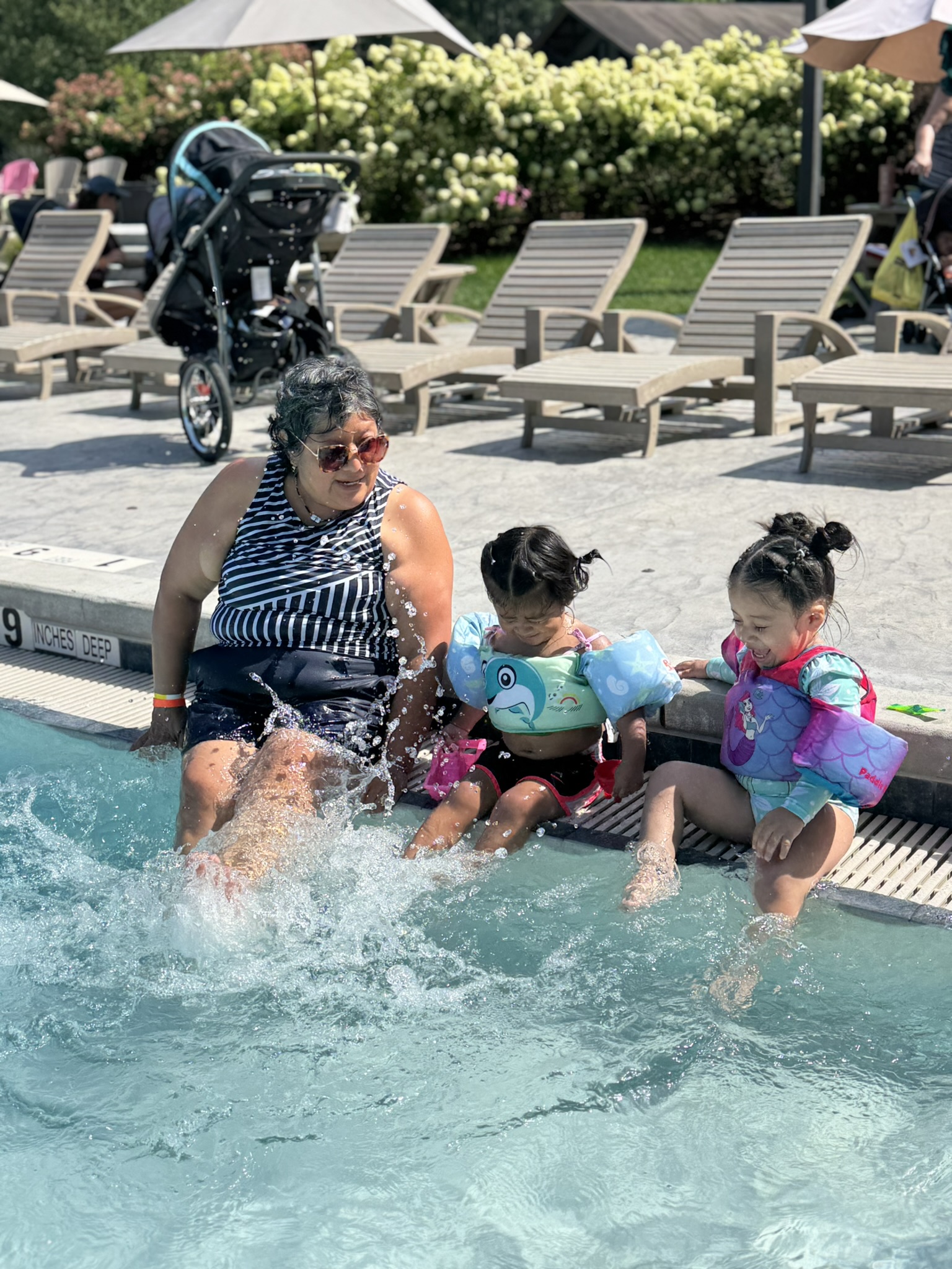 A grandmother laughing with two young girls splashing in the pool at camp
