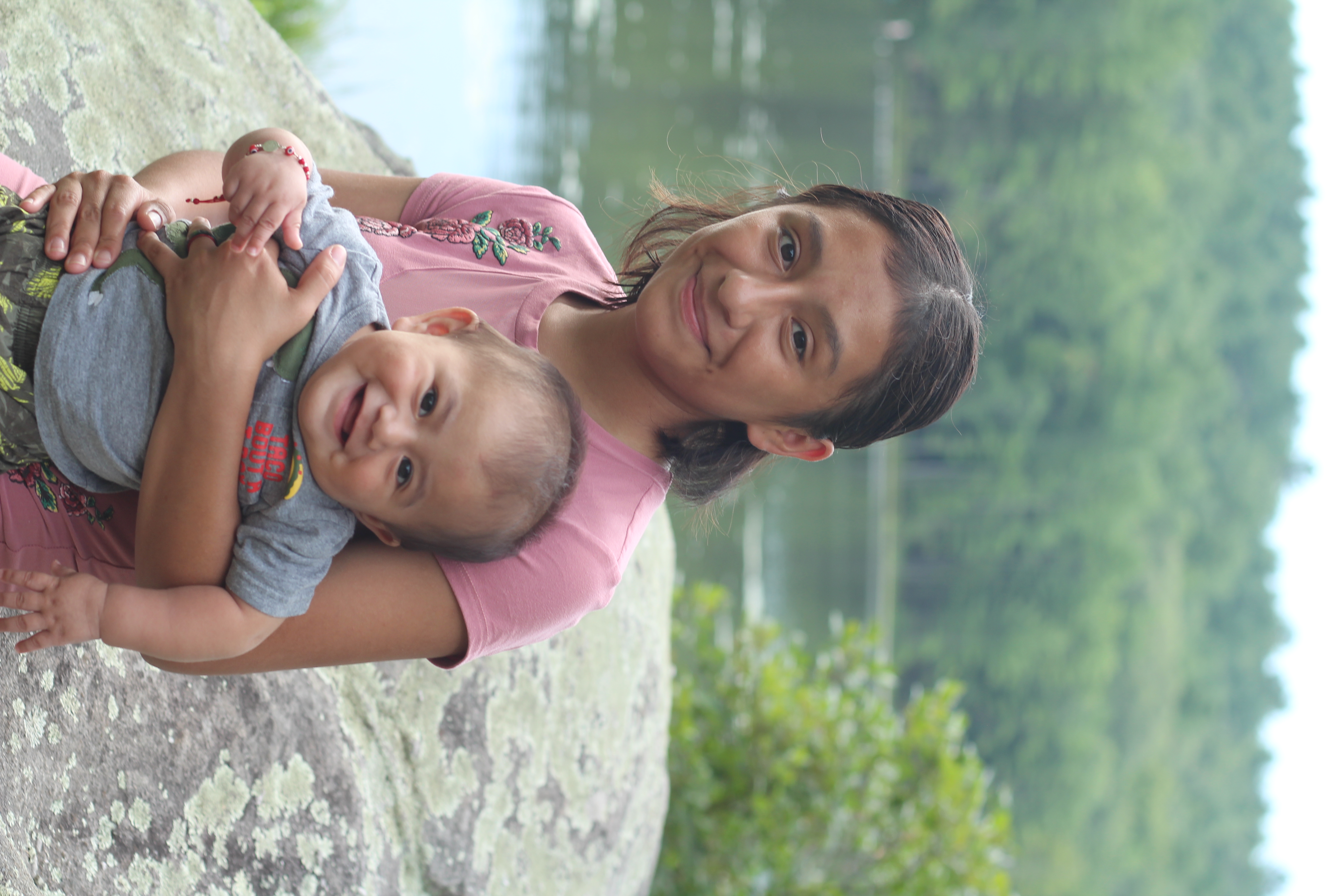 An older girl holding a baby by a lake at camp